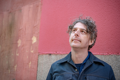 Portrait of an attractive middle aged man in front of a brightly colored wall in a city.