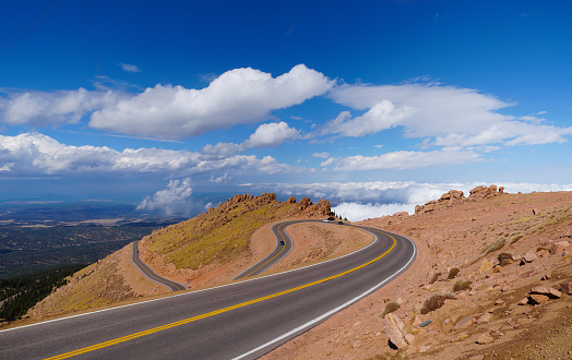 Highway through tall spires and mesas of rich dark red rugged mountains near Monument Valley in Arizona and Utah of western USA in North America. This is part of the Navajo Indian Nation in USA.  Nearest cities are Phoenix, Arizona, Salt Lake City, Utah, Denver and Durango, Colorado.