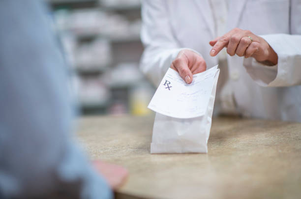 Pharmacist Holding Out a Packaged Prescription stock photo A pharmacist in a white lab coat holds out a processed and packaged prescription as he explains how to properly and safely take the medication.  The patient is dressed casually and standing on the other side of the counter.  Only the patient and pharmacists hands can be seen. prescription medicine stock pictures, royalty-free photos & images