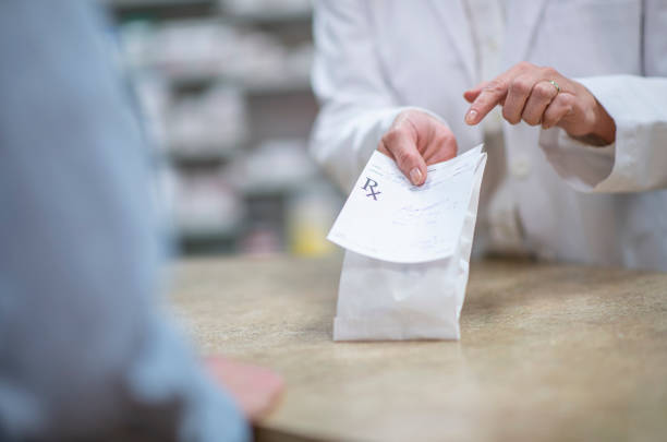 Pharmacist Holding Out a Packaged Prescription stock photo A pharmacist in a white lab coat holds out a processed and packaged prescription as he explains how to properly and safely take the medication.  The patient is dressed casually and standing on the other side of the counter.  Only the patient and pharmacists hands can be seen. presecriptions stock pictures, royalty-free photos & images