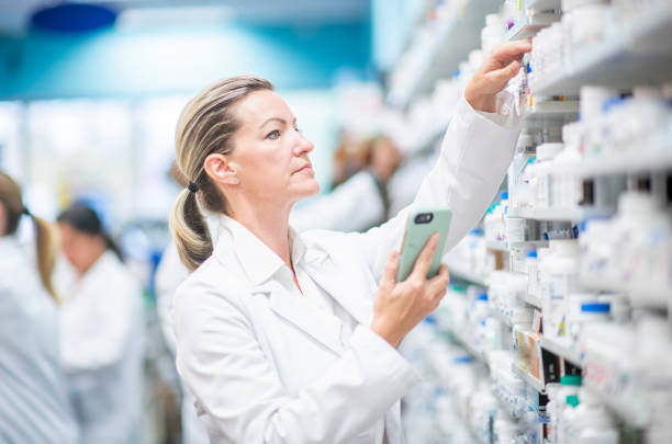 farmacéutico femenino utiliza el teléfono celular para ayudar a buscar una foto de stock con receta - pill bottle pharmacy medicine shelf fotografías e imágenes de stock