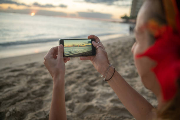 istock Young woman photographing sunset on beach using mobile phone 1194009064