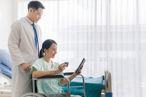 patient female using digital tablet and credit card making payment while  sitting on wheelchair at the hospital