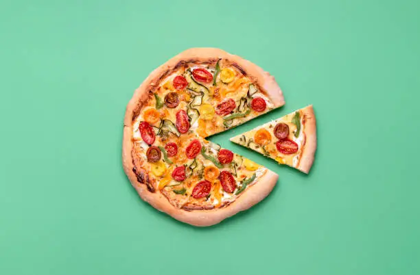 Vegetarian pizza on a green background. Pizza primavera and just one slice. Single slice of spring pizza. Italian meal. Cherry tomato pizza.