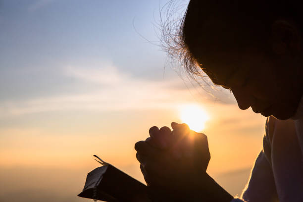 Silhouette of christian young woman praying with a  cross and open the bible at sunrise, Christian Religion concept background. Silhouette of christian young woman praying with a  cross and open the bible at sunrise, Christian Religion concept background. kneeling stock pictures, royalty-free photos & images