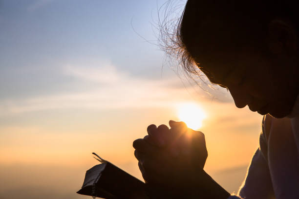 sylwetka chrześcijańskiej młodej kobiety modląc się z krzyżem i otworzyć biblię o wschodzie słońca, religia chrześcijańska tło koncepcji. - rosary beads bible prayer beads catholicism zdjęcia i obrazy z banku zdjęć