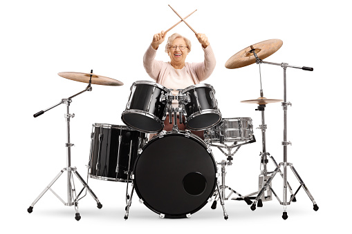 Senior woman holding crossed drumsticks with a set of drums isolated on white background
