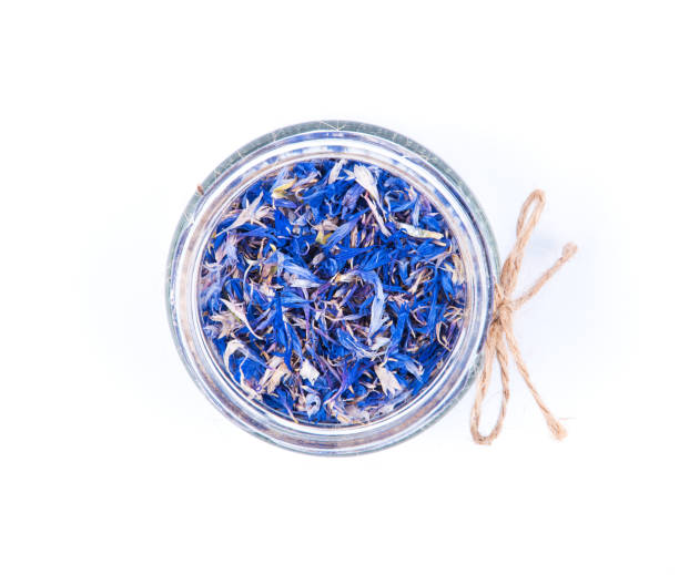 Top view of blue cornflower centaurea dried petals in a glass jar decorated with bow isolated on white background. Natural medicine and cosmetic concept.