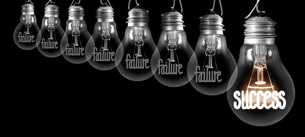 Group of shining and dimmed light bulbs with fibers in a shape of Failure and Success concept words isolated on black background.