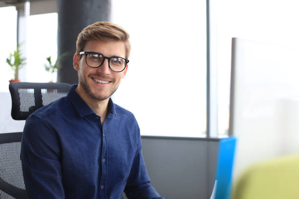 istock Good looking young business man looking at camera and smiling while sitting in the office. 1194055171