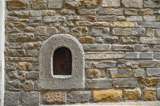 Close-up of a wine window (buchetta del vino), used in the past to sell wine directly to passers-by, on the old stone wall of an ancient building in the historic centre of Florence, Tuscany, Italy