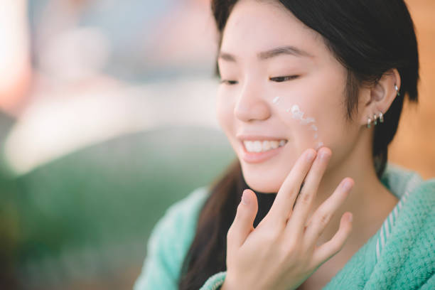 an asian chinese teenager girl applying moisturiser facial cream on hand and face - teenager teenagers only one teenage girl only human face imagens e fotografias de stock