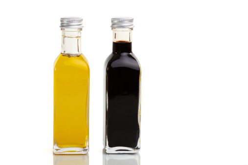 Extra virgin olive oil and balsamic vinegar bottles isolated on reflective white background. Rosemary twigs, garlic cloves, and mixed peppercorns are around the bottles and complete the composition. The composition is at the right of an horizontal frame leaving useful copy space for text and/or logo at the left. Predominant colors are yellow, black and white. High resolution 42Mp studio digital capture taken with Sony A7rII and Sony FE 90mm f2.8 macro G OSS lens