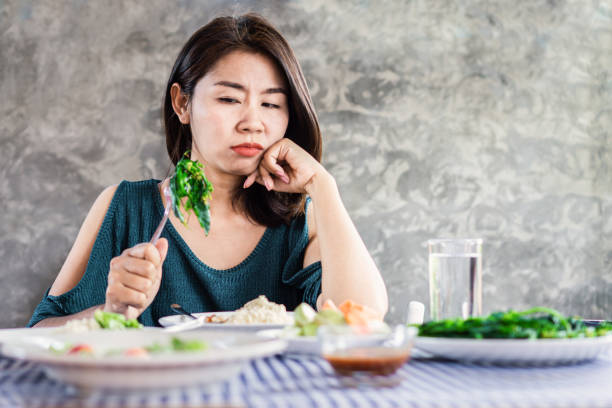 femme asiatique malheureuse sur l'alimentation à la différence de manger la nourriture saine et le légume - dieting food rejection women photos et images de collection