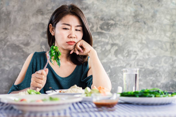 несчастная азиатская женщина на диете в отличие от здоровой пищи и овощей - dieting food rejection women стоковые фото и изображения