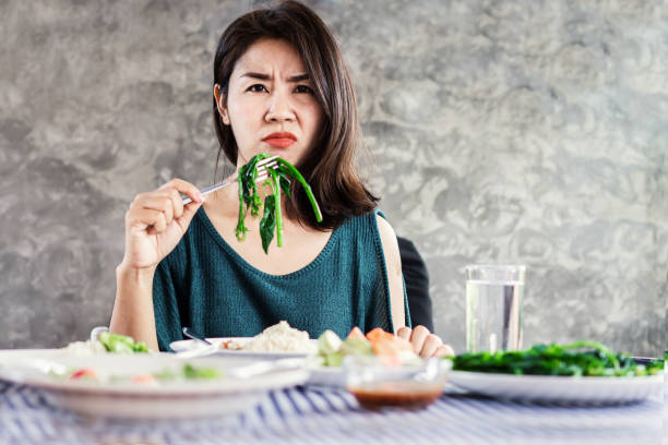 femme asiatique malheureuse sur l'alimentation à la différence de manger la nourriture saine et le légume - dieting food rejection women photos et images de collection