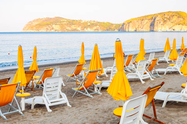 istock White plastic and metal construction with yellow fabric deckchairs together with yellow umbrellas on the sand beach of Tyrrhenian sea with mountains on background in Italy 1194072721