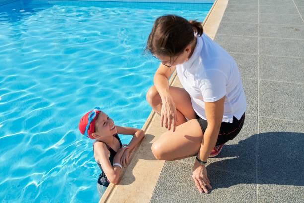 屋外プールの近くで水着の帽子とゴーグルで女の子と話す女性トレーナー - secrecy instructor exercising individuality ストックフォトと画像