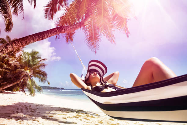 mulher nova que relaxa no hammock sobre a praia - hammock comfortable lifestyles relaxation - fotografias e filmes do acervo