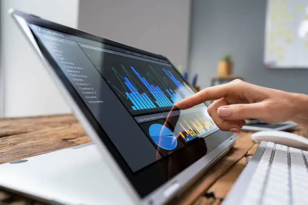 Close-up Of A Businesswoman's Hand Analyzing Graph On Laptop At Workplace