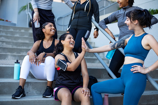 Group of multiracial female friends give each other high five after a good training session. Females in sportswear enjoying after completing exercise session on stairs in the city in morning.