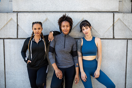 Portrait of three sportspeople standing together against wall. Healthy young women standing together after workout in the morning.