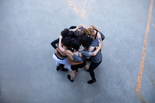Directly above view of diverse group of females standing together in huddle after training session. Multi-ethnic group of women in a huddle with their arms around shoulder.