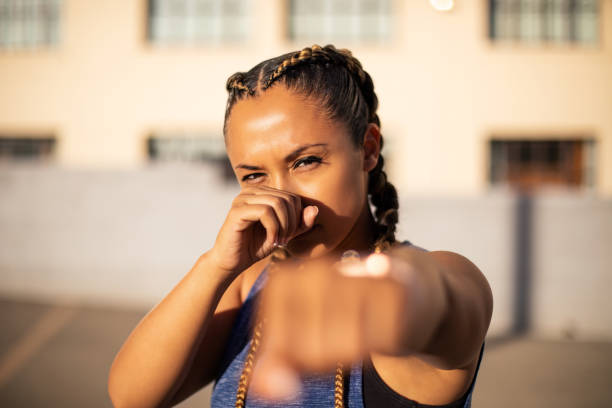 Athletic woman in boxing stance outdoors Portrait of determined young athletic woman in sportswear standing in boxing stance with hands and fists, looking at camera. boxing sport stock pictures, royalty-free photos & images