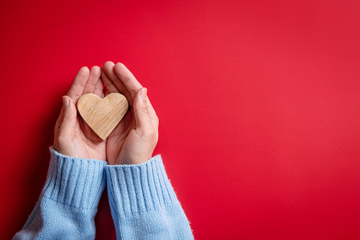 Female hands giving wood heart on red background, top view, copy space.