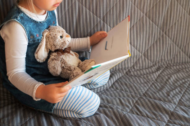 Little girl reading favorite book at home. Little girl reading favorite book at home with her toy rabbit. picture book stock pictures, royalty-free photos & images