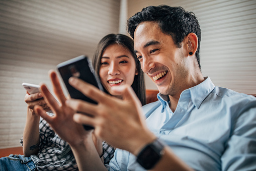 Young man and woman using smart phone in the living room making selfie