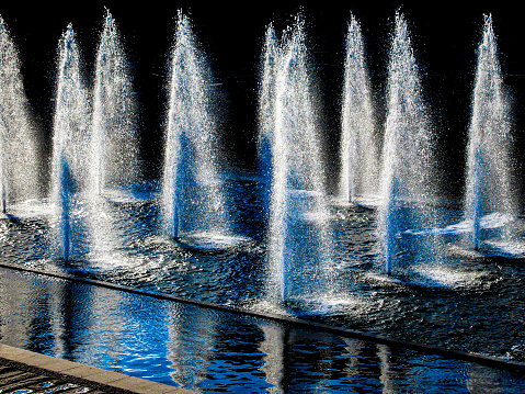 Water fountain with symmetrical water flow and splash with reflection in water with a dark background