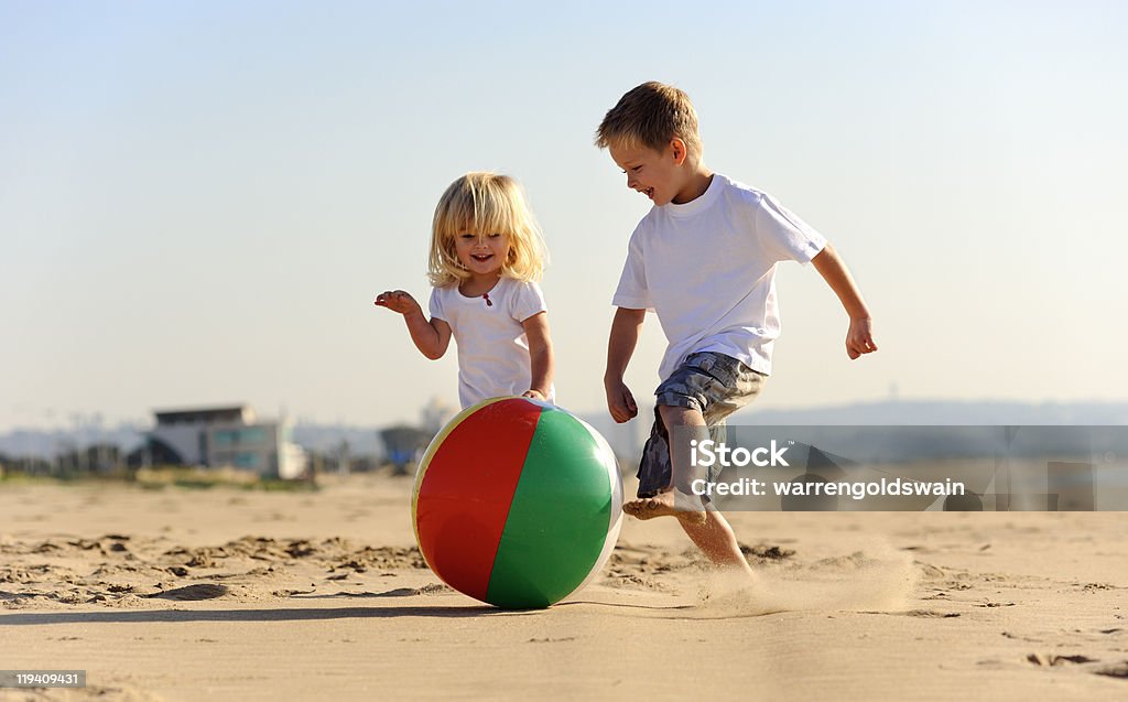 A boy and a girl playing ball at the beach Beautiful brother and sister play with a beach ball outdoors Beach Stock Photo