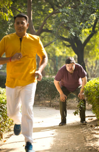 istock Fitness instructor jogging while exhausted fat man is taking a break at park 1194095486