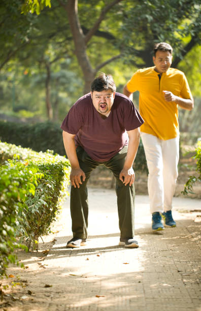 istock Fitness instructor jogging while exhausted fat man is taking a break at park 1194095509