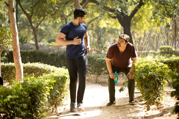 istock Fitness instructor jogging while exhausted fat man is taking a break at park 1194095678
