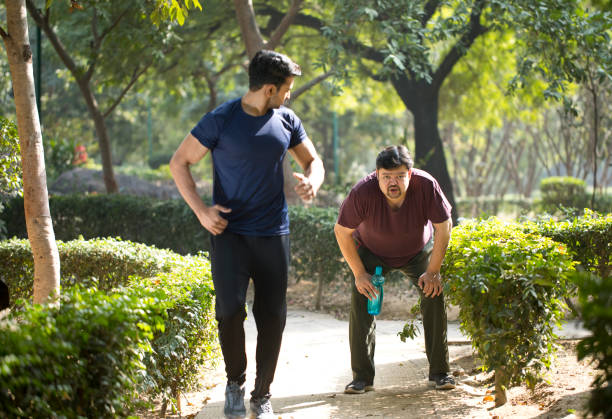istock Fitness instructor jogging while exhausted fat man is taking a break at park 1194095692