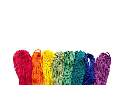 Colored threads for embroidery, seven colors of the rainbow lie in a row on a white background