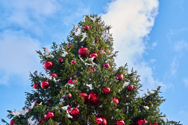 istock Decorated Christmas tree with big red balls and white birds against blue sky 1194100919