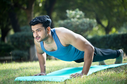 Fit young man doing push ups on grass field at park