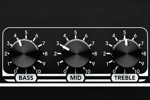 Close up detail of sound equalizer control knobs of a black guitar amplifier. Bass, mid and treble knobs.