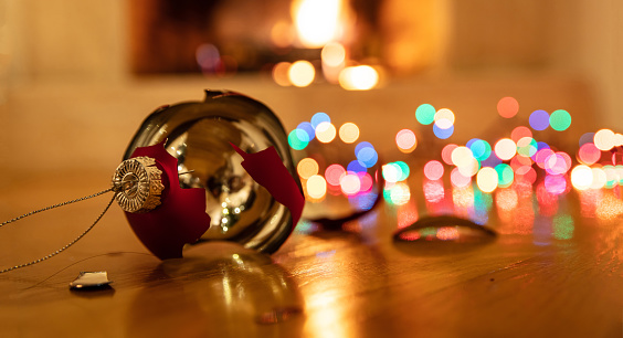 Christmas ball broken. Xmas holiday decoration, lights glowing, blur burning fireplace background, reflections on the wood floor