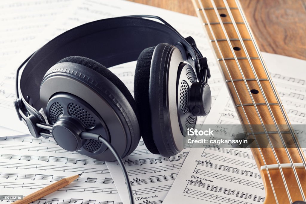 Professional studio headphones and bass guitar neck on music sheets background Professional studio headphones and bass guitar neck on music sheets background. Concept of music recording or composing. Close up view. Headphones Stock Photo