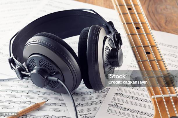 Professional Studio Headphones And Bass Guitar Neck On Music Sheets Background Stock Photo - Download Image Now
