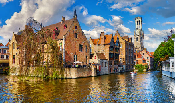 Bruges, Belgium. Ancient medieval european city. View Bruges, Belgium. Ancient medieval european city. View at tower Belfort van Brugge and vintage building at bank of Rozenhoedkaai channel river. Panoramic view with blue sky and clouds. Famous tourist bell tower tower stock pictures, royalty-free photos & images