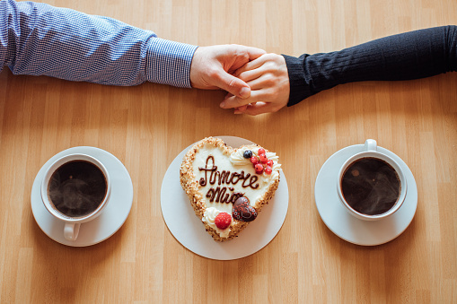 Plano, vista superior del hombre y la mujer cogidos de la mano mientras bebe café con pastel de crema con la inscripción italiana 