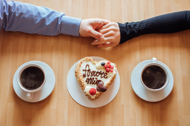 lay piatto, vista dall'alto di uomo e donna che si tengono per mano mentre bevono caffè con torta alla crema con la scritta italiana "amore mio" - coffee couple italy drinking foto e immagini stock