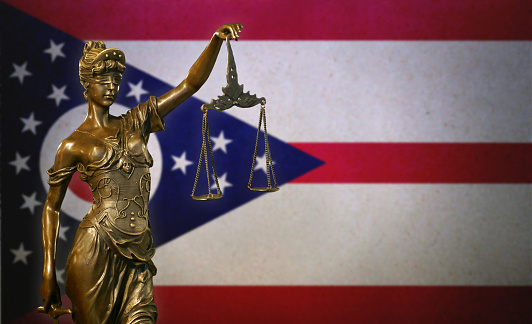 Close-up of a small bronze statuette of Lady Justice before a flag of Ohio.