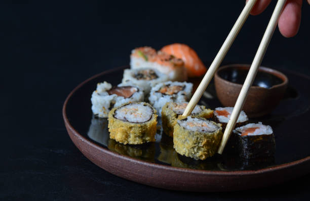 cierre de un rollo de sushi con palillos. comida japonesa, roll con salmón, niguiri, panecillos calientes. - niguiri sushi fotografías e imágenes de stock