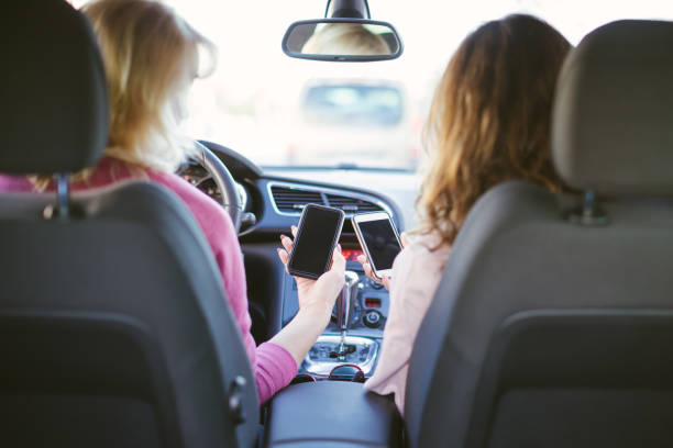 vista posteriore di due donne sedute in auto con gli smartphone - le persone si perdono e stanno cercando la strada giusta sulla mappa mobile - donna che usa il telefono mentre guida - car phone foto e immagini stock